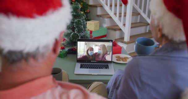 クリスマスに顔のマスクに女性の友人とラップトップでビデオ通話で幸せなシニア白人カップル コロナウイルスのクリスマス お祭り 通信技術は19のパンデミックを克服しました — ストック動画