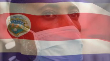 Covid 19 salgını sırasında yüzü maskeli bir adamın üzerinde sallanan Costa Rica bayrağının animasyonu. küresel covid 19 salgın konsepti dijital olarak oluşturulmuş video.