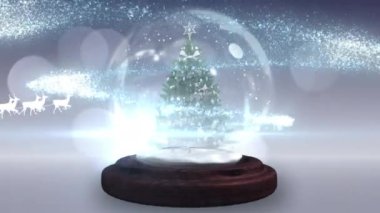 Kar küresindeki Noel ağacına karşı ren geyikleri tarafından çekilen kızaklı Noel Baba. Noel şenliği ve kutlama konsepti