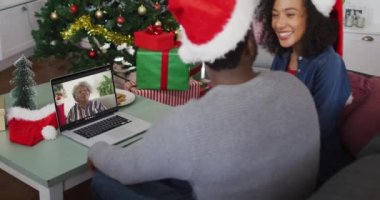 Noel Baba şapkası takan Afrikalı Amerikalı bir çift Noel 'de evde dizüstü bilgisayarlarına video çağrısı yapıyor. Noel zamanı covid 19 salgınında sosyal mesafeler