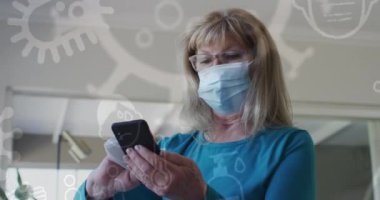 Yüz maskesi takan, akıllı telefonu dezenfekte eden Kafkasyalı yaşlı bir kadın için Coperid 19 ikonu. küresel covid 19 salgın konsepti dijital olarak oluşturulmuş video.