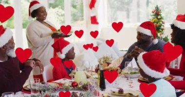 Noel 'de akşam yemeği sırasında mutlu Afro-Amerikan ailesinin üzerinde yüzen kalplerin animasyonu. Noel, kış, gelenek ve kutlama konsepti dijital olarak oluşturulmuş video.