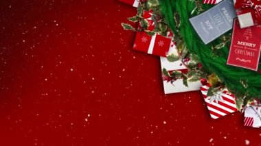 Yılbaşı çelenkleri, kartlar ve kırmızı arka planda hediyeler üzerine yağan kar. Noel şenliği ve kutlama konsepti