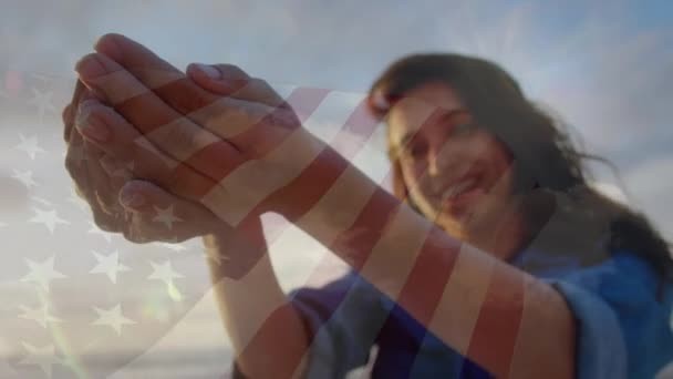 ビーチで楽しんでいる女性の上にウサの旗を振るアニメーション 愛国心とお祝いの概念デジタルで生成されたビデオ — ストック動画