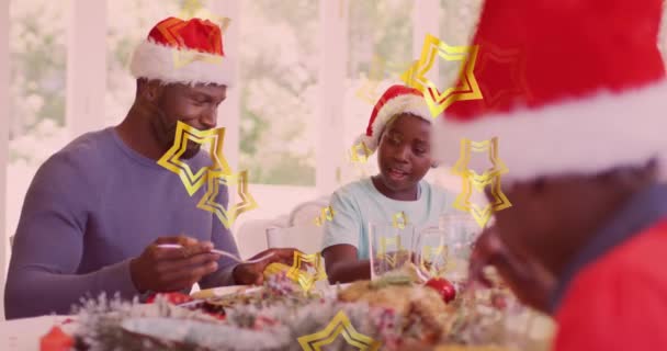明星在非洲裔美国父亲和儿子头上的动画 他们戴着圣诞大礼帽 吃着圣诞大餐 圣诞节 传统和庆祝概念数字制作的视频 — 图库视频影像