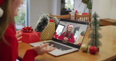 Laptop 'taki beyaz kadın Noel zamanı mutlu bayan arkadaşıyla görüntülü konuşma yapıyor. Noel, şenlik ve iletişim teknolojisi.