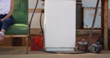 Akıllı telefondan konuşan melez bir kadın benzin istasyonunda benzin pompasının yanında oturuyor. ulaşım, petrol ve yakıt tedarik iş konsepti dijital olarak üretilen video.