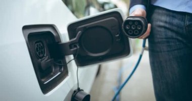 Beyaz kadının orta kısmı elektrikli araba şarj ediyor. Elektrikli araba, yeşil enerji, eko güç, sürdürülebilirlik ve CO2 azaltımı için her şarj istasyonu.