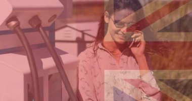 Akıllı telefon kullanan ve elektrikli araba şarj eden gülümseyen beyaz kadın için İngiltere bayrağı. Elektrikli araba, yeşil enerji, eko güç, sürdürülebilirlik ve CO2 azaltımı için her şarj istasyonu.