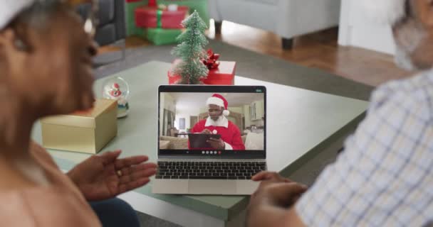 クリスマスの時間にサンタクロースとノートパソコンのビデオ通話で幸せなアフリカ系アメリカ人のシニアカップル クリスマスやお祭りや通信技術は — ストック動画