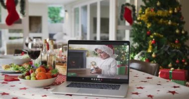 Noel Baba şapkalı, dizüstü bilgisayarlı mutlu beyaz çocuk Noel masasında yatıyor. Noel, şenlik ve iletişim teknolojisi.