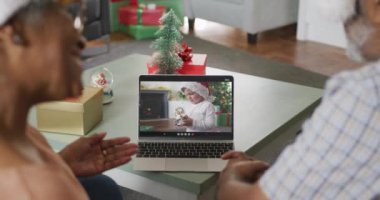 Noel 'de Noel Baba şapkalı çocukla görüntülü konuşma yapan mutlu Afro-Amerikan çift. Noel, şenlik ve iletişim teknolojisi.