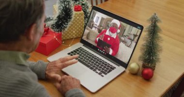 Noel 'de Noel Baba' nın maskeli olduğu videodaki Kafkasyalı kıdemli mutlu adam. Coronavirus covid 19 salgını sırasında Noel, şenlik ve iletişim teknolojisi.