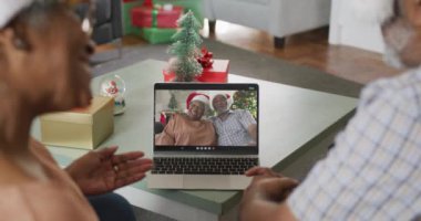 Mutlu Afro-Amerikan çifti dizüstü bilgisayarında son sınıf arkadaşlarıyla Noel zamanı görüntülü konuşma yapıyor. Noel, şenlik ve iletişim teknolojisi.