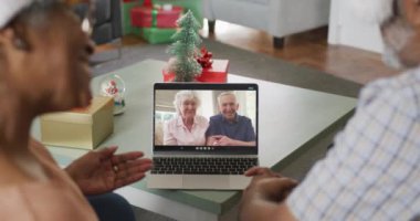 Mutlu Afro-Amerikan çifti dizüstü bilgisayarında son sınıf arkadaşlarıyla Noel zamanı görüntülü konuşma yapıyor. Noel, şenlik ve iletişim teknolojisi.