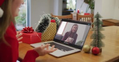 Laptop 'taki beyaz kadın Noel zamanı mutlu bayan arkadaşıyla görüntülü konuşma yapıyor. Noel, şenlik ve iletişim teknolojisi.
