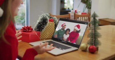 Laptop 'taki beyaz kadın Noel zamanı mutlu bir aileyle görüntülü görüşme yapıyor. Noel, şenlik ve iletişim teknolojisi.