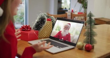 Dizüstü bilgisayardaki beyaz kadın Noel Baba 'yla Noel zamanı video görüşmesi yapıyor. Noel, şenlik ve iletişim teknolojisi.