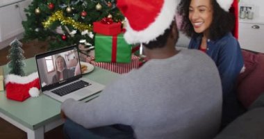 Mutlu Afro-Amerikan çifti dizüstü bilgisayarında yüz maskeli bir bayanla Noel 'de görüntülü konuşma yapıyor. Coronavirus covid 19 salgını sırasında Noel, şenlik ve iletişim teknolojisi.