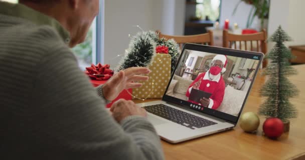 一位白种人老人带着非洲裔美国人带着面具在笔记本电脑上拨打圣诞视频电话 圣诞节 节日和通信技术 — 图库视频影像
