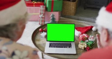 Noel Baba şapkalı son sınıf Kafkasyalı çift yeşil ekranlı, dizüstü bilgisayarlı noel mesajı gönderiyorlar. Noel, şenlik ve iletişim teknolojisi.