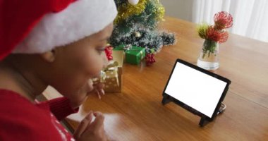 Noel Baba şapkalı Afrikalı Amerikalı bir kadın dizüstü bilgisayarla noel için video görüşmesi yapıyor ve ekranında da bir kopya alanı var. Noel, şenlik ve iletişim teknolojisi.
