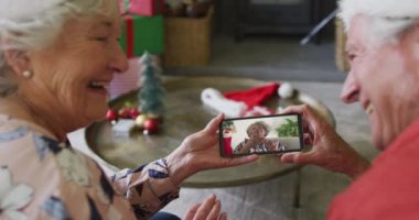 Üst düzey Kafkasyalı çift, ekranda gülümseyen arkadaşıyla yılbaşı videosu için akıllı telefon kullanıyor. Noel, şenlik ve iletişim teknolojisi.