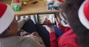 Afrika kökenli Amerikalı anne ve kız. Ekranda arkadaşlarıyla yılbaşı videosu için tablet kullanıyorlar. Noel, şenlik ve iletişim teknolojisi.