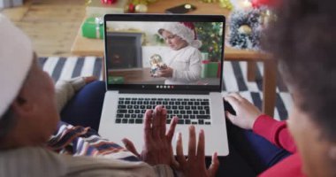 Afrika kökenli Amerikalı anne ve kız. Ekrandaki çocukla yılbaşı videosu için dizüstü bilgisayar kullanıyorlar. Noel, şenlik ve iletişim teknolojisi.