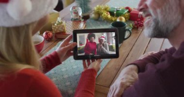 Noel Baba şapkalı beyaz bir çift Noel 'de ekranda gülümseyen bir aileyle tablet kullanıyor. Noel, şenlik ve iletişim teknolojisi.