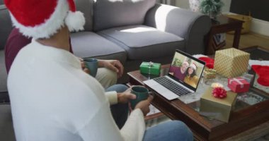 Çift ırklı baba ve oğul, ekranda gülümseyen bir çiftle yılbaşı görüntüsü için dizüstü bilgisayar kullanıyor. Noel, şenlik ve iletişim teknolojisi.