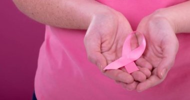Beyaz kadının pembe arka planlı pembe kanser farkındalığı kurdelesi taşıdığı bir video. Göğüs kanseri pozitif farkındalık kampanyası konsepti.