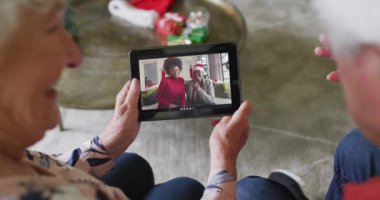 Üst düzey Kafkasyalı çift Noel 'de ekranda gülümseyen bir aileyle birlikte tablet kullanıyor. Noel, şenlik ve iletişim teknolojisi.