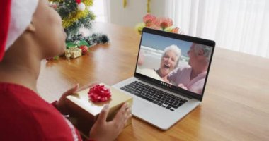 Noel Baba şapkalı Afro-Amerikalı bir kadın Noel 'de ailesini ekranda görmek için dizüstü bilgisayar kullanıyor. Noel, şenlik ve iletişim teknolojisi.