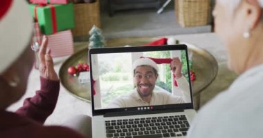 Kıdemli çeşitli bayan arkadaşlar, ekranda gülümseyen arkadaşlarıyla yılbaşı videosu için dizüstü bilgisayar kullanıyorlar. Noel, şenlik ve iletişim teknolojisi.