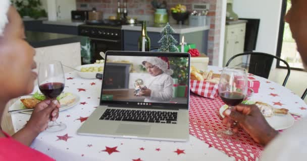 画面上の男の子とクリスマスビデオコールのためのラップトップを使用してワインでアフリカ系アメリカ人のカップルを笑顔 クリスマスやお祭りや通信技術は — ストック動画
