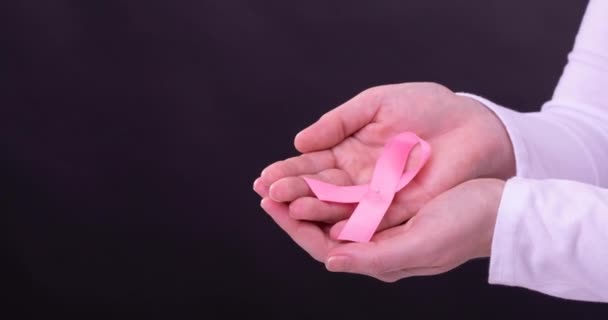在黑色背景上拿着粉色癌症意识带的高加索女人的手的视频 乳腺癌积极认识运动概念 — 图库视频影像