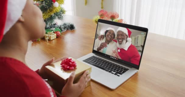 クリスマスのビデオ通話のためのラップトップを使用してサンタの帽子を持つアフリカ系アメリカ人の女性 画面上の家族 クリスマスやお祭りや通信技術は — ストック動画