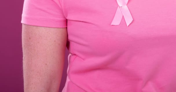 ピンクの背景をしたピンクの癌の啓発リボンを身に着けている白人女性の中央部のビデオ 乳がん認知キャンペーンのコンセプト — ストック動画