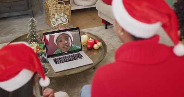 スクリーン上の家族とクリスマスのビデオ通話のためのラップトップを使用してサンタの帽子を持つアフリカ系アメリカ人の家族 クリスマスやお祭りや通信技術は — ストック動画