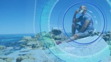 Yükleme çemberinin ve pusulanın animasyonu deniz kıyısında oturan Afrika kökenli Amerikalı son sınıf öğrencisinin üzerinde. spor ve sağlıklı, aktif emeklilik yaşam tarzı ve teknoloji konsepti dijital olarak oluşturulmuş video.