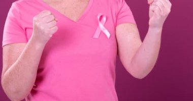 Beyaz kadın, yumruklarını kaldırmış pembe kanser farkındalığı kurdelesi takıyor. Göğüs kanseri pozitif farkındalık kampanyası konsepti.