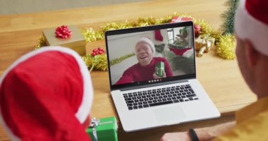 Beyaz bir baba ve oğlu Noel 'de ekranda gülümseyen bir arkadaşıyla birlikte dizüstü bilgisayar kullanıyor. Noel, şenlik ve iletişim teknolojisi.