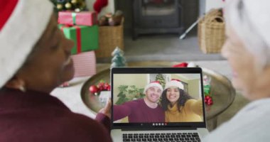 Kıdemli çeşitli bayan arkadaşlar, ekranda gülümseyen arkadaşlarıyla yılbaşı videosu için dizüstü bilgisayar kullanıyorlar. Noel, şenlik ve iletişim teknolojisi.