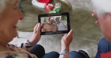 Üst düzey Kafkasyalı çift, ekranda gülümseyen yaşlı bir çiftle Noel videosu için tablet kullanıyor. Noel, şenlik ve iletişim teknolojisi.