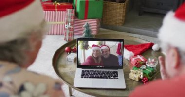 Üst düzey Kafkasyalı çift, ekranda gülümseyen bir çiftle yılbaşı görüntüsü için laptop kullanıyor. Noel, şenlik ve iletişim teknolojisi.