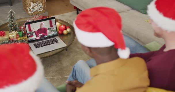 スクリーン上の男とクリスマスビデオ通話のためのラップトップを使用してサンタの帽子を持つ多様な家族 クリスマスやお祭りや通信技術は — ストック動画