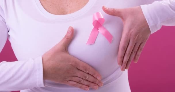 ピンクの背景をしたピンクの癌の啓発リボンを身に着けている白人女性の中央部のビデオ 乳がん認知キャンペーンのコンセプト — ストック動画