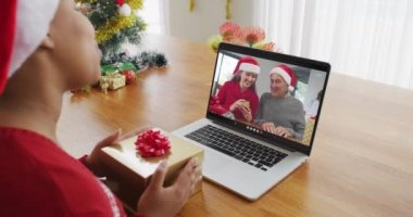 Noel Baba şapkalı Afro-Amerikalı bir kadın Noel 'de ailesini ekranda görmek için dizüstü bilgisayar kullanıyor. Noel, şenlik ve iletişim teknolojisi.