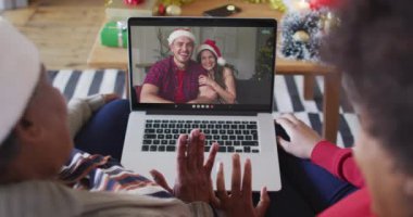 Afrika kökenli Amerikalı anne ve kız. Ekrandaki çiftle yılbaşı videosu için dizüstü bilgisayar kullanıyorlar. Noel, şenlik ve iletişim teknolojisi.